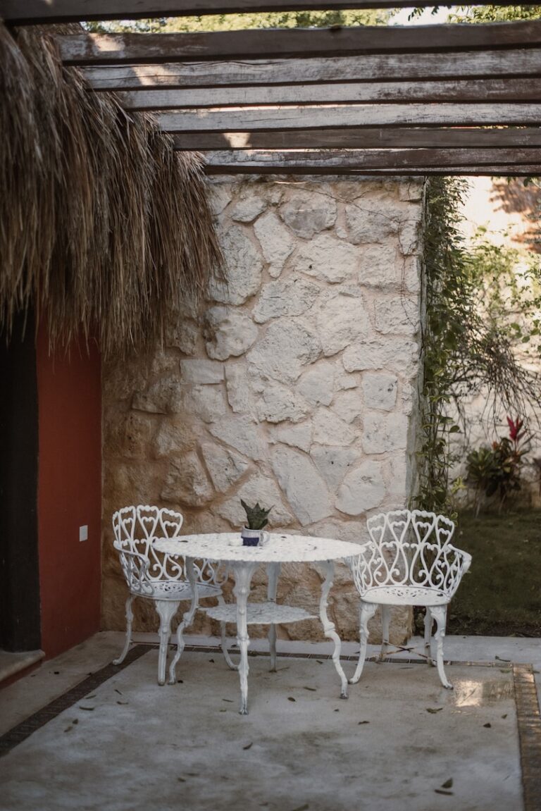 two white chairs and a table in front of a stone wall